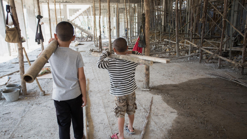 Two young boys carrying heavy poles in a construction site